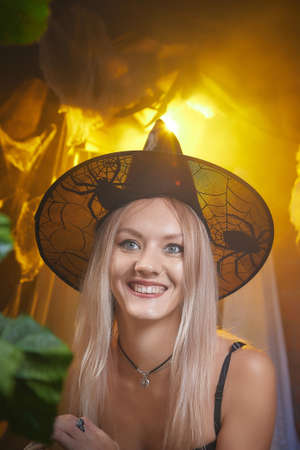 Young woman looking like witch having fun on Halloween in a dark room with yellow light and smoke. Carnival concept and Halloween partyの写真素材
