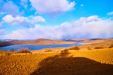 Beautiful natural view of the landscape with the shore with yellow grass, lake, and blue sky with...