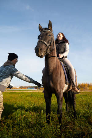 Kirov, Russia - October 04, 2020: Woman riding a horse in filed and coach near in autumn day and blue sky backgroundのeditorial素材