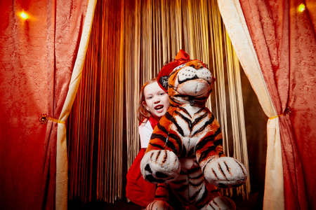 Small girl during a stylized theatrical circus photo shoot in a beautiful red location with tiger....