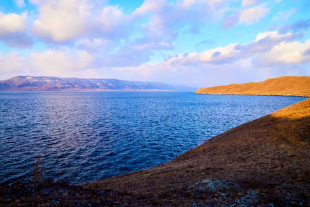 Beautiful natural view of the landscape with the shore with yellow grass, lake, and blue sky with...