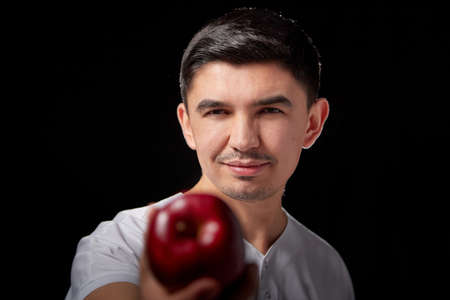 A young man who is a medical doctor in a white medical uniform and with red apple poses against a black background in the studioの写真素材