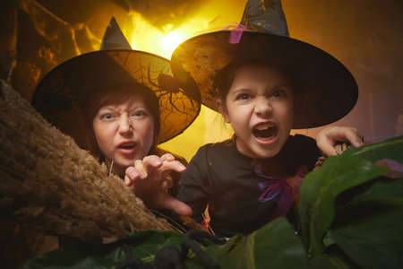 Mom and daughter in costumes for a holiday of halloween in dark decoration and with nice yellow light. Funny nice family during carnival in the roomの写真素材