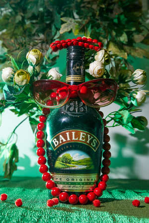 Kirov, Russia - July 23, 2020: Red beads, bracelet, green surface and a bottle of good liquor. The concept of rich, secure lifeのeditorial素材