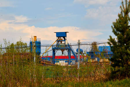 Building of plant or factory in rural place framed by tree branches and shrubs and blue sky with...