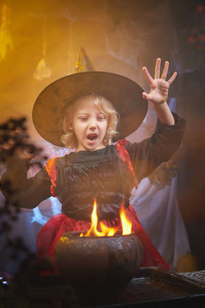 Cute little girl with curly blonde hair in costume for witch in the room decorated fot Halloweenの写真素材