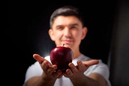 A young man who is a medical doctor in a white medical uniform and with red apple poses against a black background in the studioの写真素材
