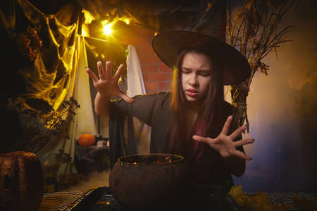 Young girl looking like witch having fun on Halloween in a dark room with yellow light and smoke. Teenager in Carnival and Halloween partyの写真素材