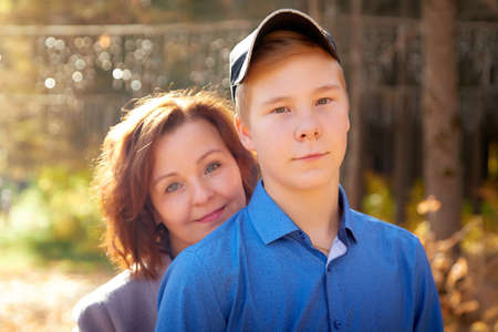 Mother and adult son in autumn park or forest in sunny day. Happy family walking outdoorsの写真素材