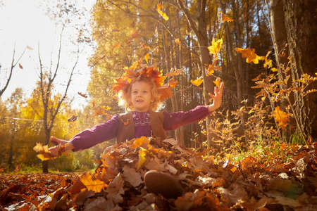 Portrait of young little girl with blonde curly hair in an autumn park on a yellow and orange leaf backgroundの写真素材