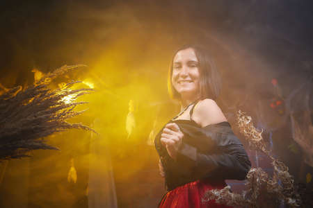 Young woman looking like witch having fun on Halloween in a dark room with yellow light and smoke....