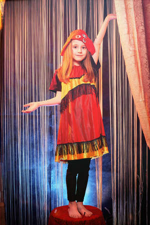 Small girl during a stylized theatrical circus photo shoot in a beautiful red location. Young model posing on stage with curtainの写真素材