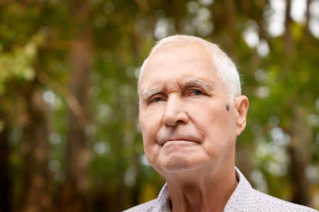 Porter of a gray-haired elderly man on a green background in the forest or in the park. Grandfather...