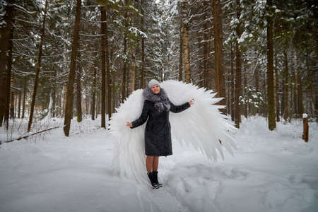 Woman with angel wings with white feathers in the cold russian forest in winter with snow covered trees. A model poses during a photo shoot in Siberia in Russiaの写真素材