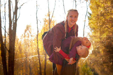 Two young little girl and his mother with blonde hair in an autumn park on a yellow and orange leaf background. Family walking in forestの写真素材