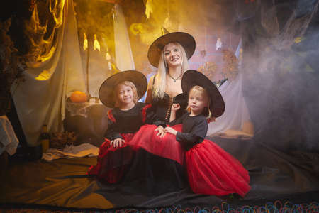 Mom and daughters in costumes for a holiday of halloween in dark decoration and with nice yellow light. Funny nice family during carnival in the roomの写真素材