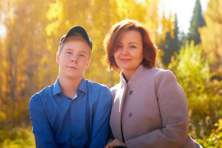 Mother and adult son in autumn park or forest in sunny day. Happy family walking outdoorsの写真素材