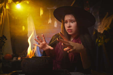 Young girl looking like witch having fun on Halloween in a dark room with yellow light and smoke. Teenager in Carnival and Halloween partyの写真素材