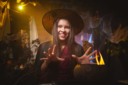 Young girl looking like witch having fun on Halloween in a dark room with yellow light and smoke. Teenager in Carnival and Halloween partyの写真素材