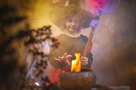 Cute little girl with curly blonde hair in costume for witch in the room decorated fot Halloweenの写真素材