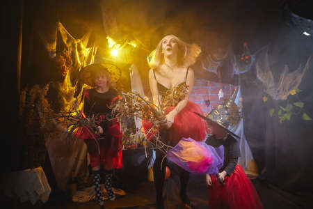 Mom and daughters in costumes for a holiday of halloween in dark decoration and with nice yellow...