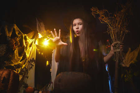 Young girl looking like witch having fun on Halloween in a dark room with yellow light and smoke. Teenager in Carnival and Halloween partyの写真素材