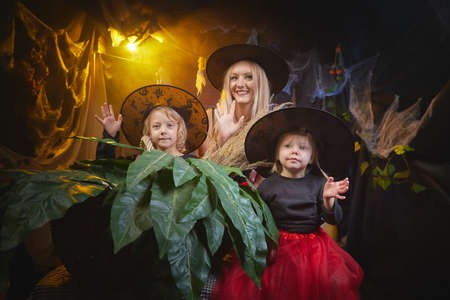 Mom and daughters in costumes for a holiday of halloween in dark decoration and with nice yellow light. Funny nice family during carnival in the roomの写真素材