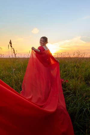 Fat plump chubby pleasant woman or girl in elegant red dres in green grass field. model posing outdoors on nature in a day or a eveningの写真素材