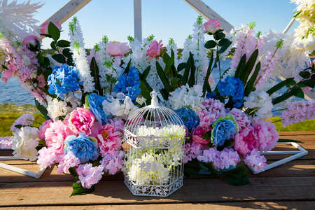 Wedding decoration with beautiful flowers and white birdcage. Decoration for getting married outdoorsの写真素材