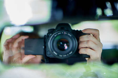 Black camera with a large lens in hands of woman. Female photographer uses a camera for a photo sessionの写真素材