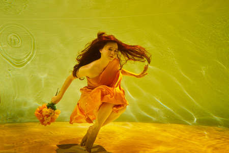 Girl in a beautiful dress under blue water. Female model posing under water in swimming poolの写真素材