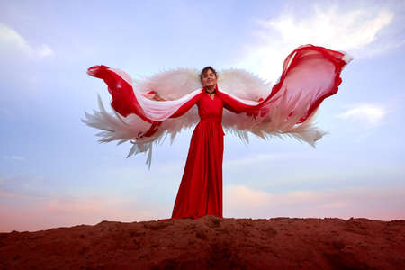 Beautiful young woman or girl with curly hair and in red dress with a light flying fabric and white...