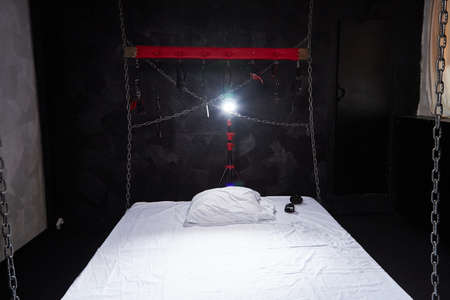 Bed with white linen and metal chains in the background. A room for bdsm sexの写真素材
