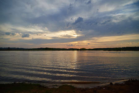 Evening sky with dramatic clouds and sunset over the river or lake. Dramatic sunset over the water