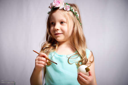 Pretty blonde little girl painting Easter eggs on white backgroundの写真素材