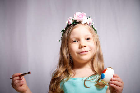Pretty blonde little girl painting Easter eggs on white backgroundの写真素材