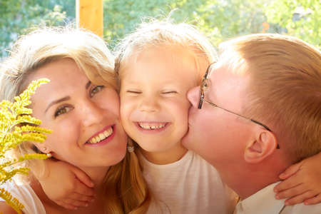 Portrait of Little blonde girl, mother and father on wooden terrace on nature or in the village and a green landscape in the background on a summer or autumn sunny day. Concept happy familyの写真素材