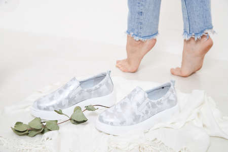 White and silver beautiful fashionable female loafers shoes on leg of girl or woman. Studio shoot on white background for magazine, website in Internet or catalogの写真素材