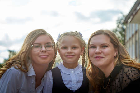 Mom and daughters who are schoolgirls in uniform near the school in Russia on September 1. Mother and sisters Girls in city in serious clothesの写真素材