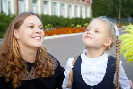 Mom and young daughter who are schoolgirl in uniform near the school in Russia on September 1. Girls...