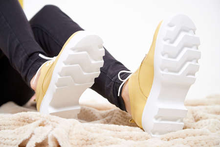 Beautiful yellow sneakers and woman legs in the studio on white background. Fashionable shooting of...
