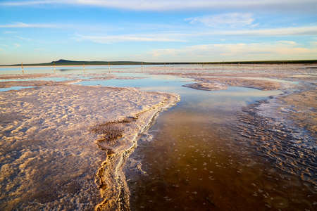 The shore of salt lake with puddles of water and sand, an endless horizon, a blue sky with white...