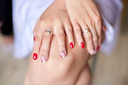 Female hands with red manicure lying on knees closeup