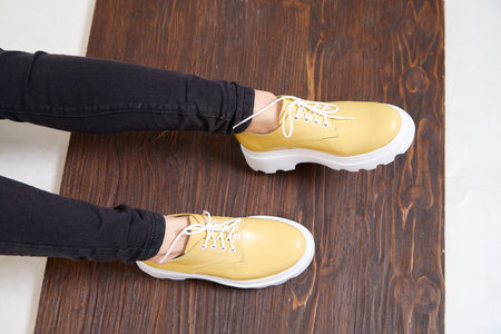 Beautiful yellow sneakers and woman legs in the studio on white background. Fashionable shooting of young girl with beautiful legsの写真素材