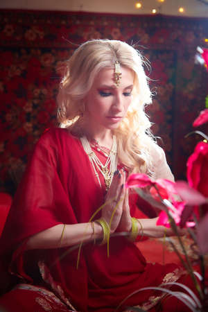 A beautiful European girl looking like an Arab woman in a red room in a harem. Photo shoot of an oriental style odalisque. A model poses in a sari as an indian woman in indiaの写真素材
