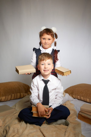 A schoolboy and schoolgirl in uniform having fun and rest with book in the room. A boy and girl during fun photo shoot about school. September 1 holiday in Russiaの写真素材