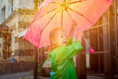 Cute little blonde girl with umbrella under rain drops on lawn in a sunny summer dayの写真素材