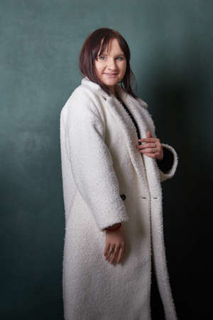 Young elegant woman in trendy white coat. Brunette hair, black dress. Fashion autumn or autumn lookbook. Model woman posing in studioの写真素材