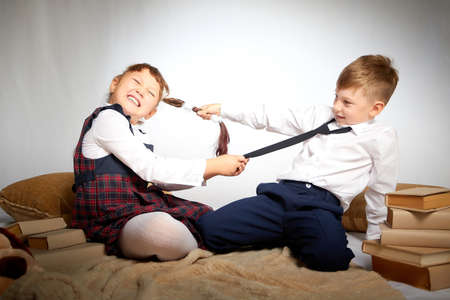 A schoolboy and schoolgirl in uniform having fight, argument, fun and rest in the room. A boy and girl during fun photo shoot about school. September 1 holiday in Russiaの写真素材