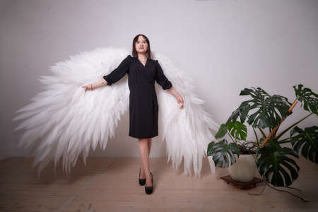 Young elegant woman in trendy black clothes with white wings. Brunette model in nice dark dress...